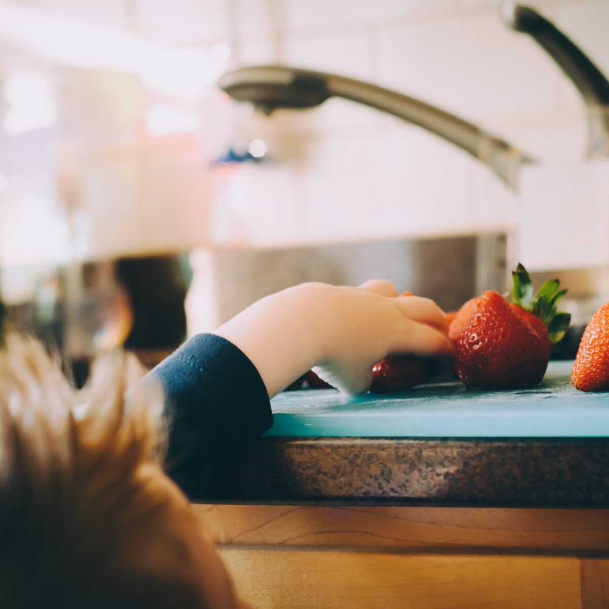 A child reaching for strawberries in the kitchen