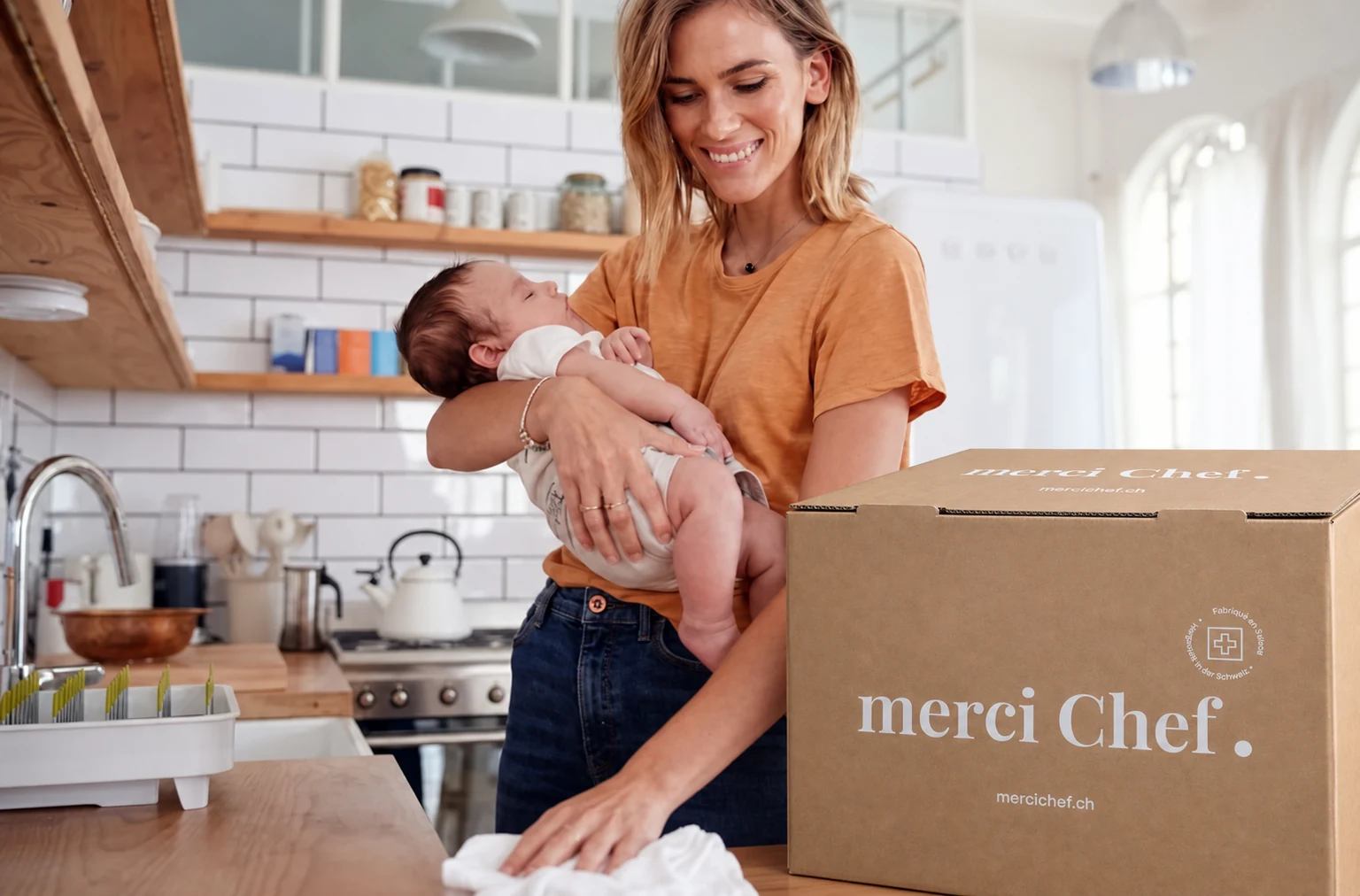 A parent with a baby and a merciChef delivery in the kitchen